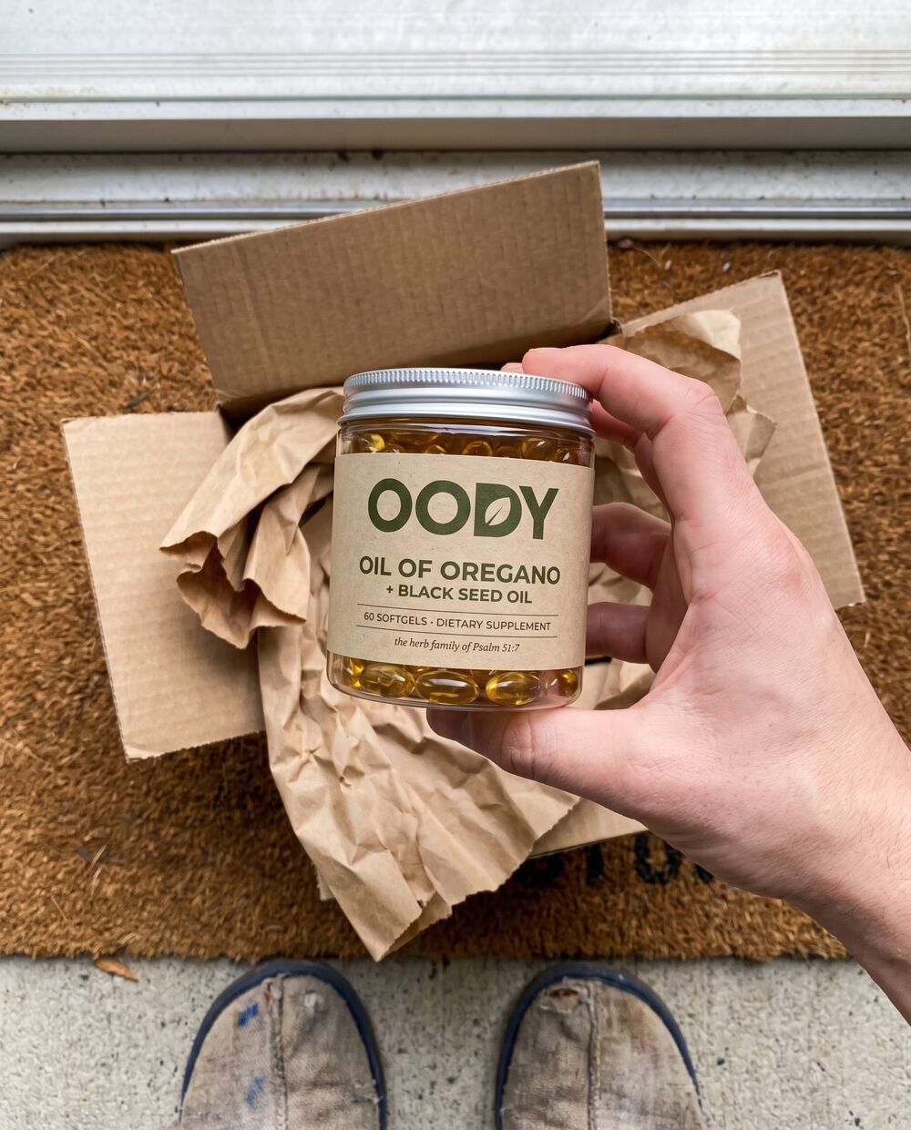 OODY jar being lifted out of a kraft mailer box on a doormat
