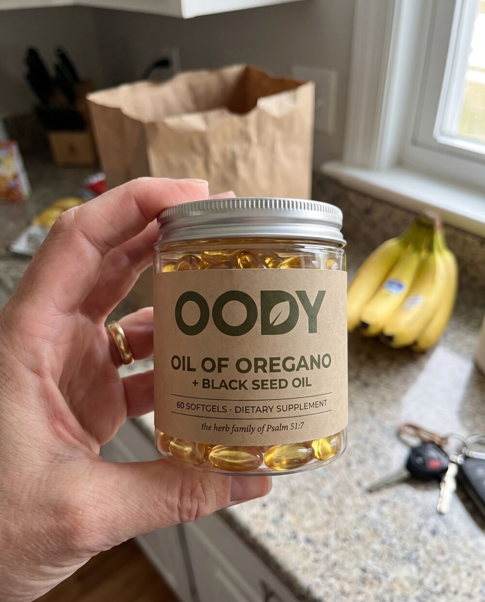 A hand holding the OODY jar above a kitchen counter with groceries