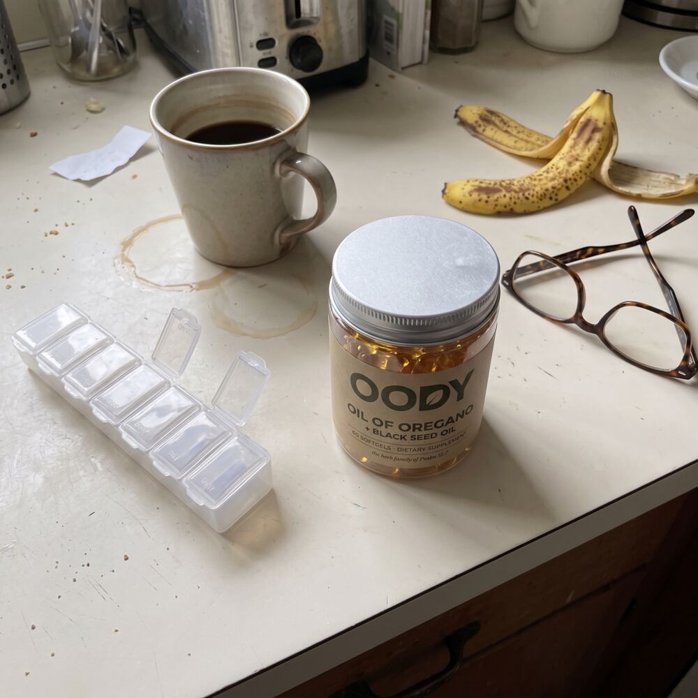 OODY jar beside a weekly pill organiser, coffee and reading glasses
