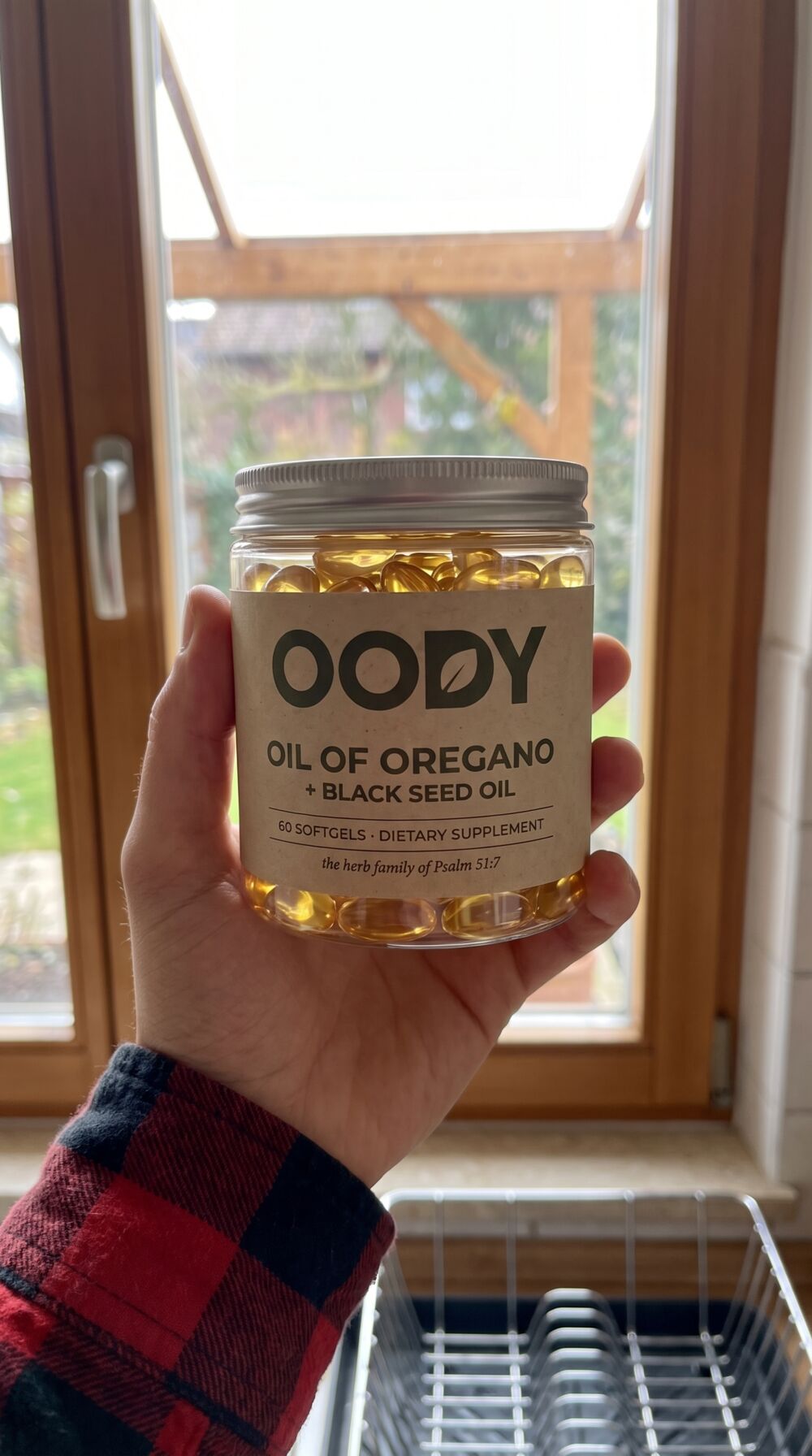 OODY jar held up to a kitchen window with light through the softgels